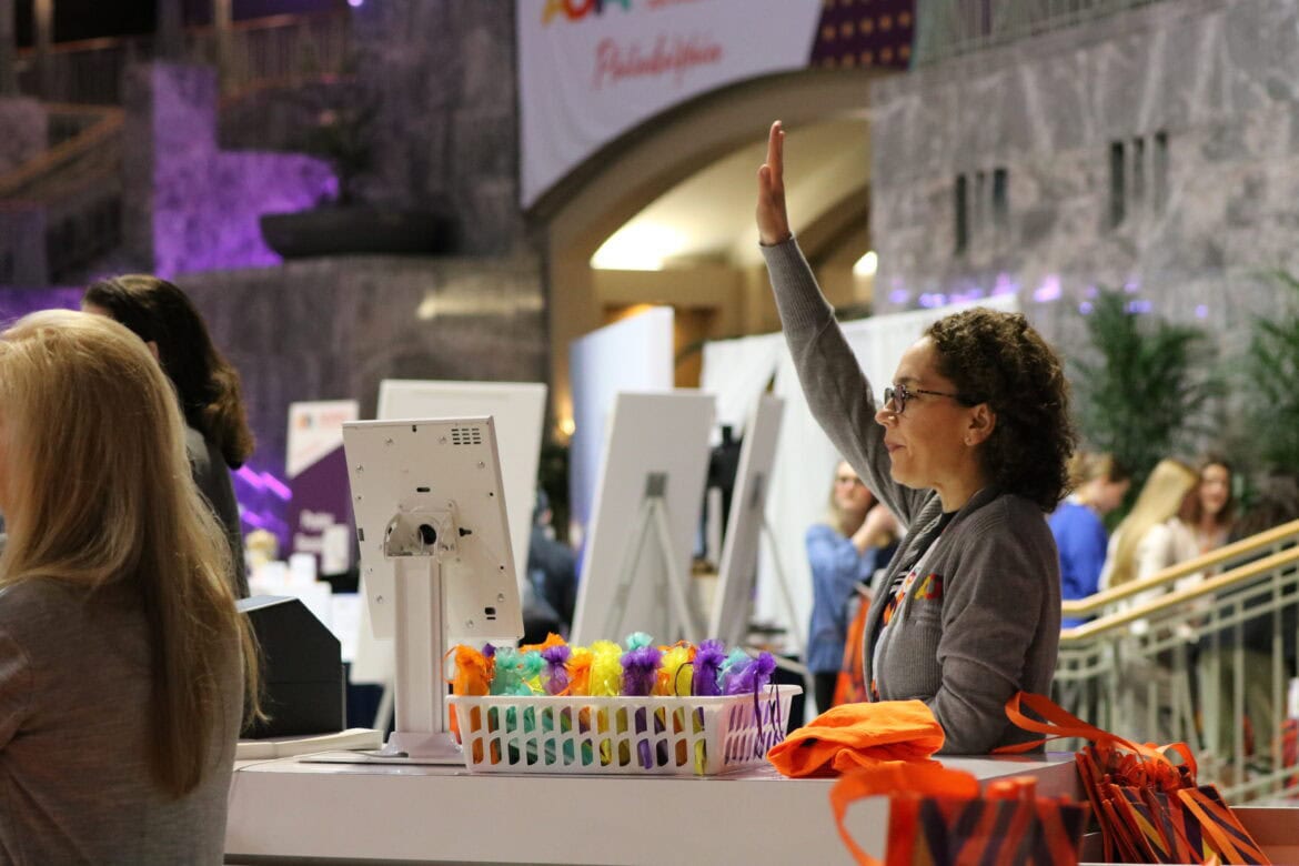 Staff member ready to help, raising her hand in the air, at a past AOTA INSPIRE.